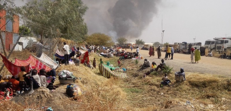 Photo: Malakal PoC residents take shelter in a UNMISS logistics area as fire engulfs their tents in the protection site (Credit: UNMISS)