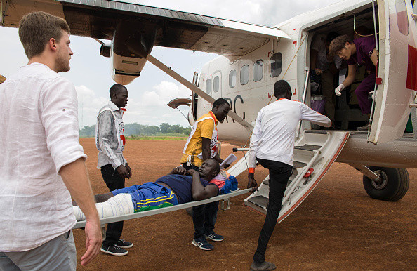 Staff of the International Committee of the Red Cross carry an injured patient to a plane to evacuate him to Juba, in Bor, South Sudan, 18 July 2017. [Photo: Stefanie Glinski/picture alliance via Getty Images]