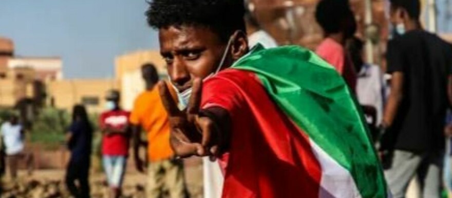 A protestor draping the Sudanese flag makes the victory sign in Khartoum before the war. (Courtesy photo)